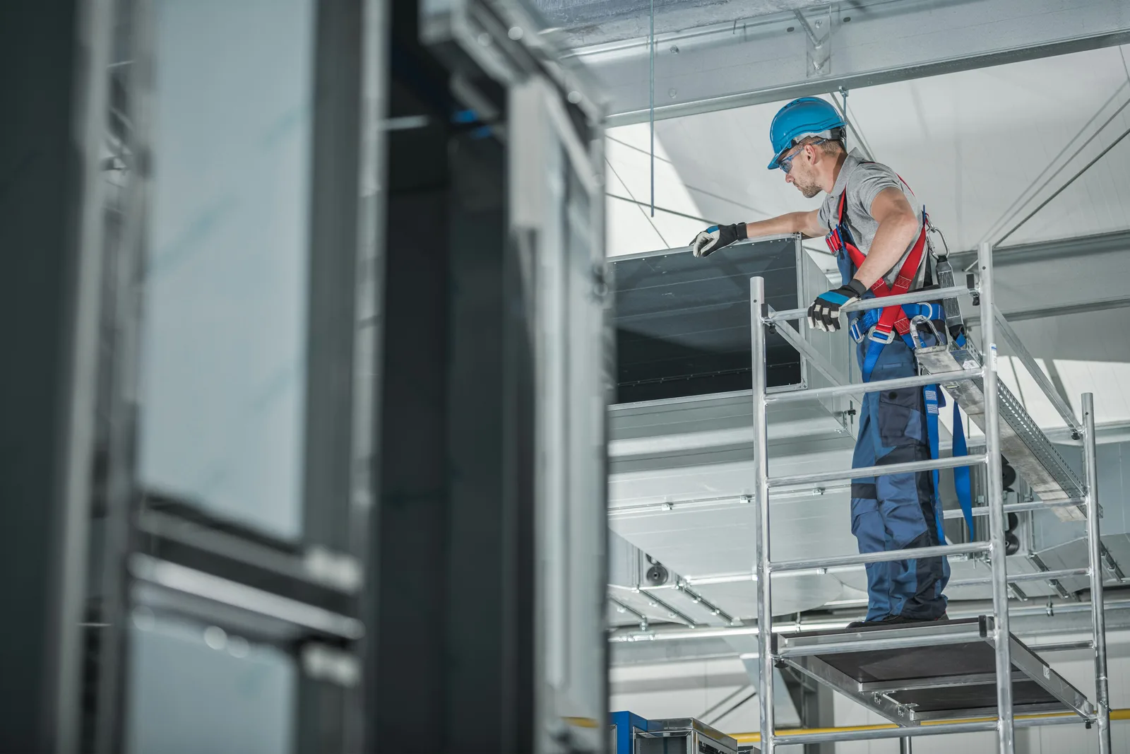 HVAC technician working on ductwork from scaffolding
